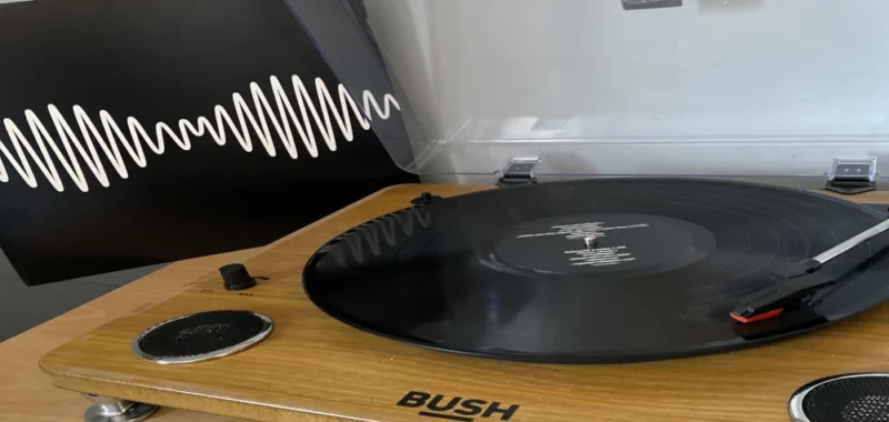 Walnut Audioengine speakers on a dark desk beside a monitor and headphones